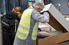 To personer i verneklær bøyer seg over en åpen pappeske med fisk i et industrirom.